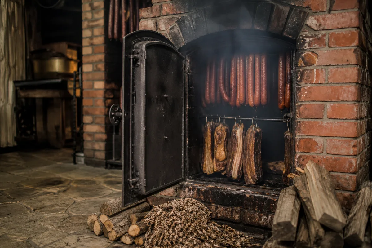 Fumoir en briques avec saucisses suspendues au-dessus de copeaux de hêtre
